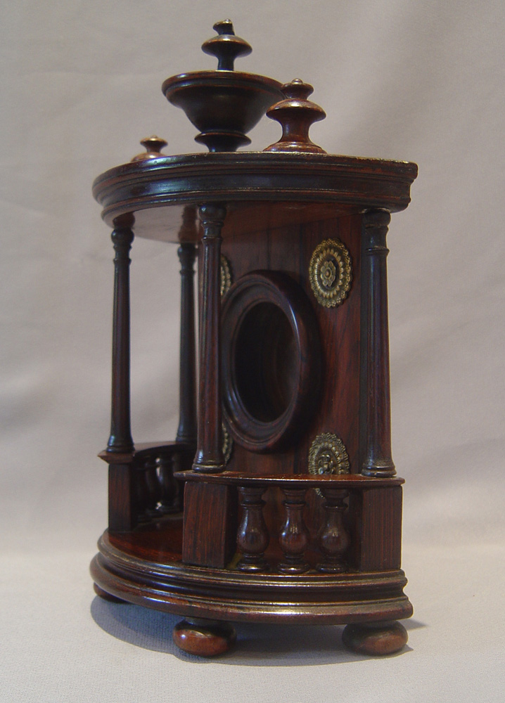 Watch stand in rosewood in bow fronted bronze mounted case with columns and finials.