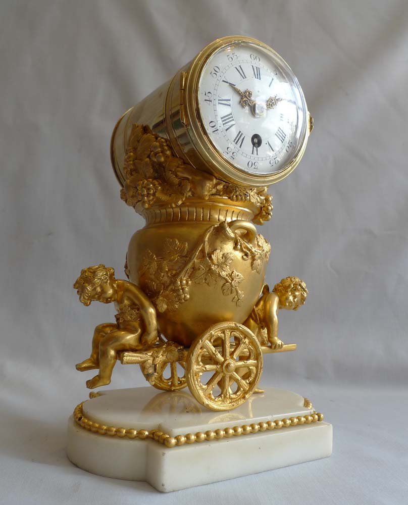 Antique French ormolu clock of two cupids pulling a cart carrying an urn full of grapes.