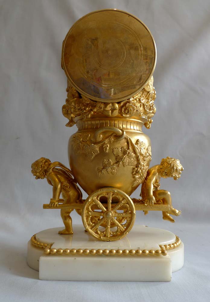 Antique French ormolu clock of two cupids pulling a cart carrying an urn full of grapes.